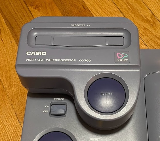 The XK-700 Magical Shop attached to the Casio Loopy. It is a large box with a large eject button and catridge slot of its own