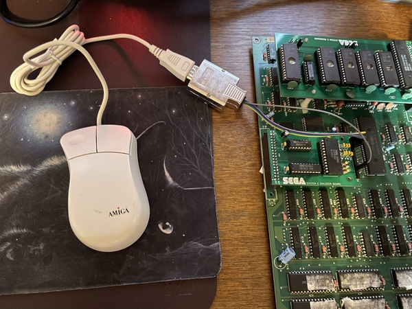 An Amiga-branded mouse sitting on the desk now attached to the circuitboard, with one more wire coming out