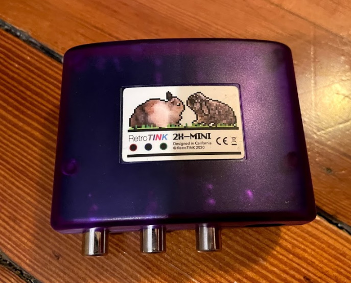 A purple RetroTINK-2X Mini's underside, showing the logo of the RetroTINK company, two bunnies