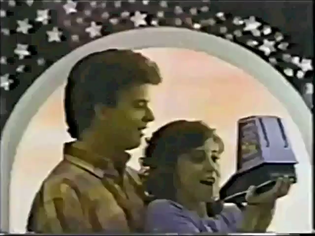 it's said this couple is still playing ms. pac-man to this very day A screen from the ad, with a couple admiring a tabletop Ms. Pac-Man like it was their child