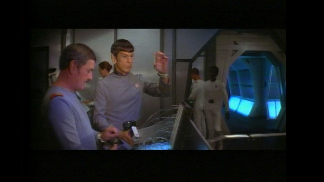 Spock holds up a vial while Scotty looks on