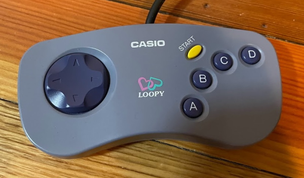 The Casio Loopy controller. It has a slight banana-like contour, a D-pad on the left, four face buttons, and a start button