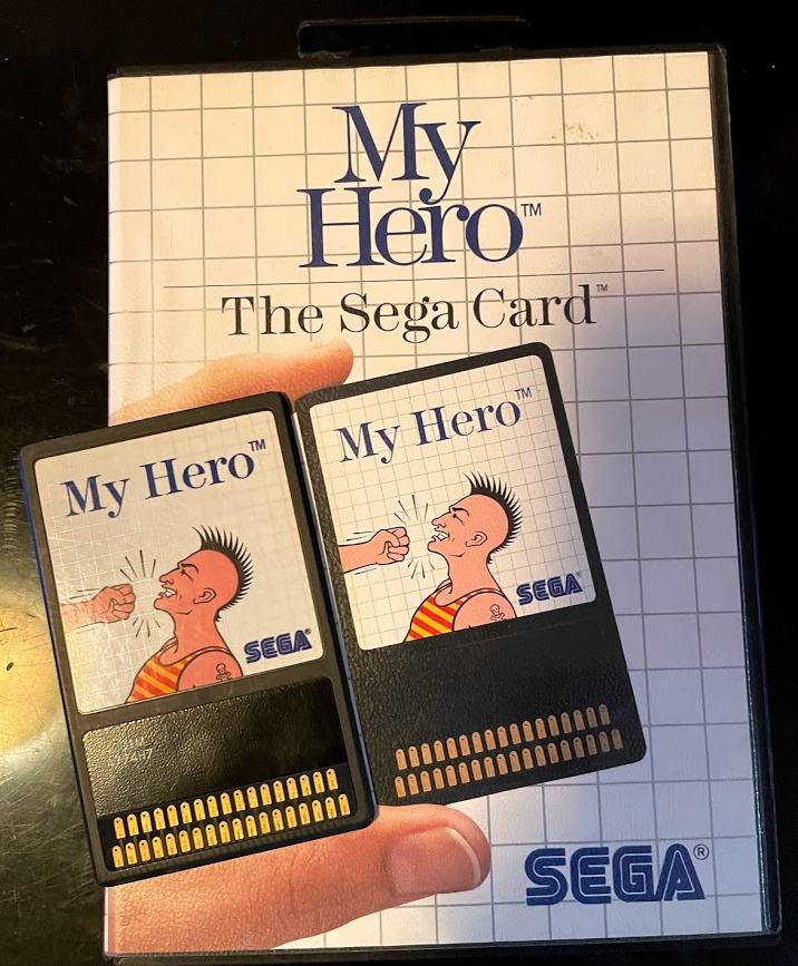 The My Hero box art. A hand holds the Sega Card. The Sega Card is placed next to it on top of the box